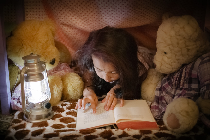 Little girl reading next to lamp