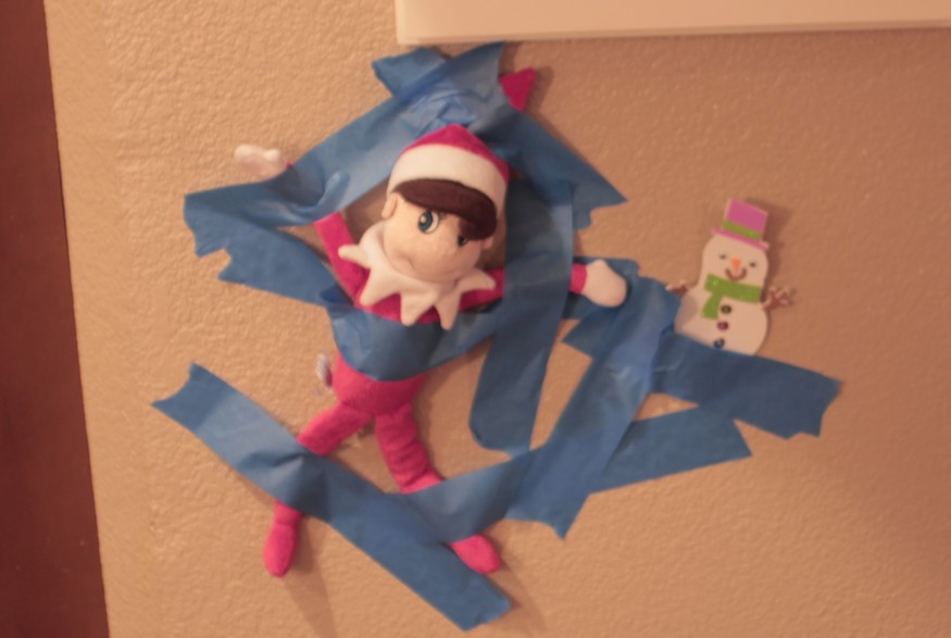 elf on the shelf taped up on a wall