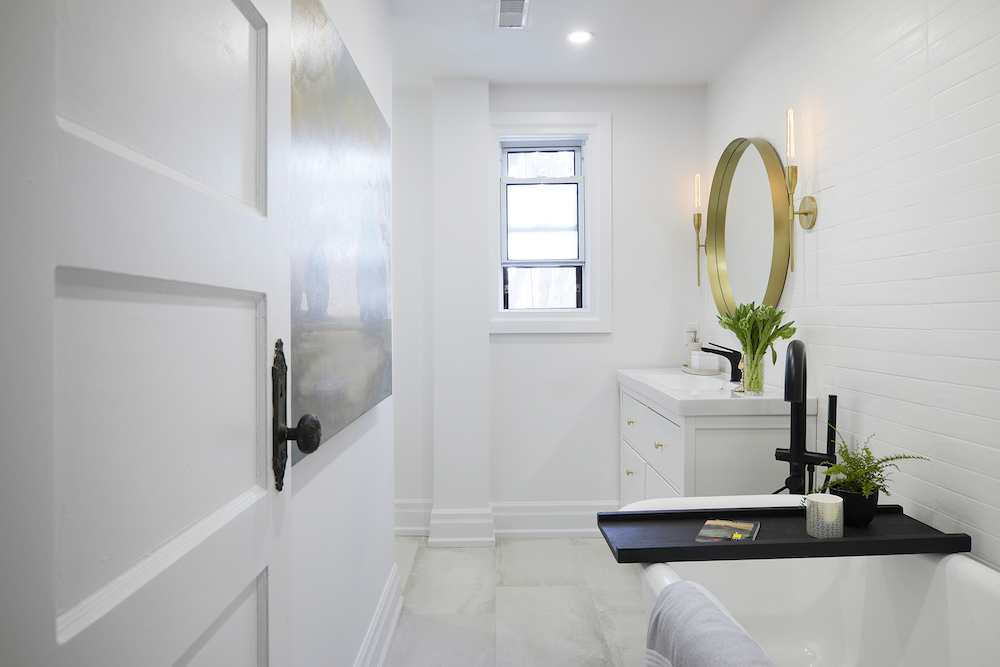 white bathroom with gold-framed mirror and black accessories on bath tub