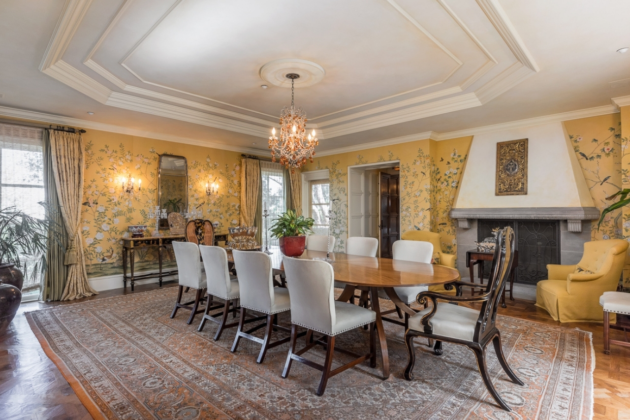 A grand living room with a ten person dining set and yellow silk wallcoverings.