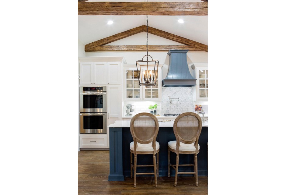 Here the exposed beams in the ceiling work to create an even cozier but barn-like effect thanks to their triangular shape. The look is then balanced out thanks to the warm blue finishes on the island and hood.