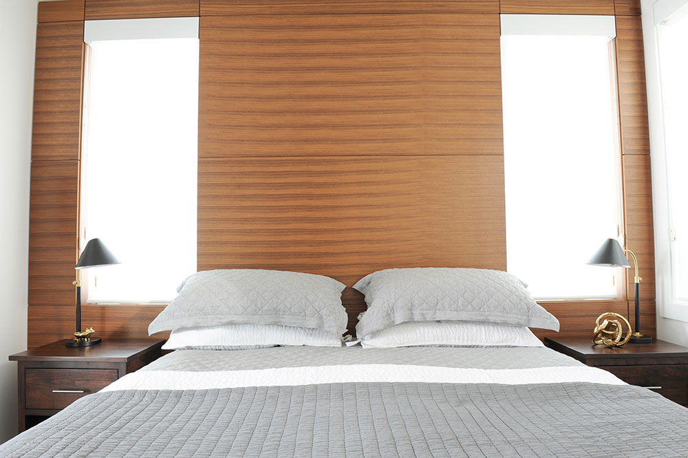 grey bed in front of walnut wall with two windows