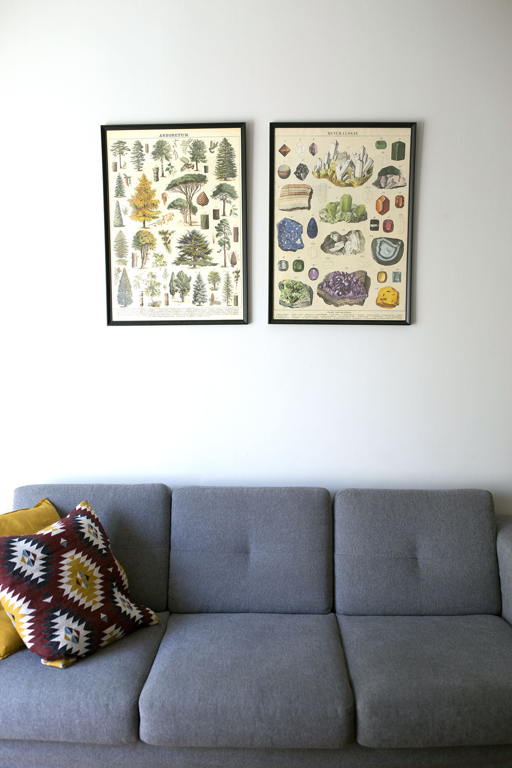 A grey mid-century modern couch with patterned throw pillows and art hanging on the wall above
