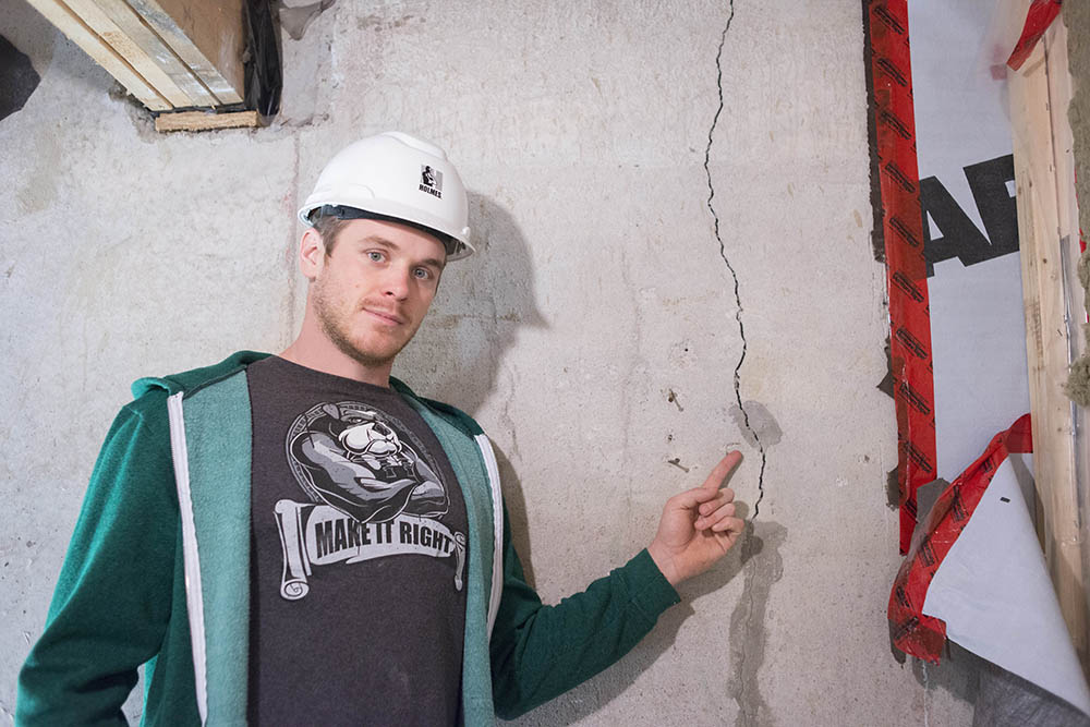 Mike Holmes Jr. pointing to a crack in a home's foundation