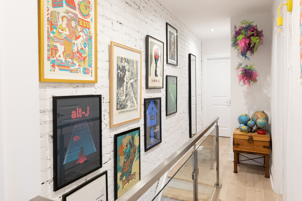 Top of stairs with gallery wall of art and white painted brick wall