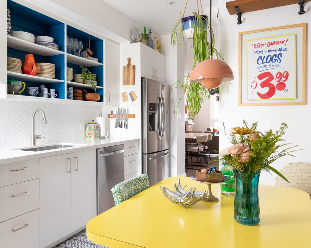 white kitchen space with yellow table and wooden shelves on wall