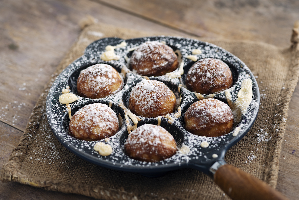 Aebleskiver pan sprinkled with powdered sugar on wooden table
