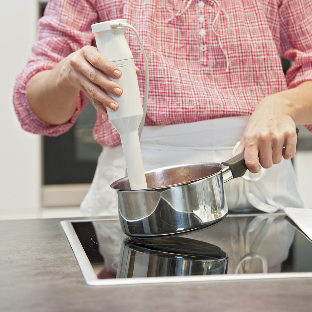 woman holding white immersion blender in silver pot on stove