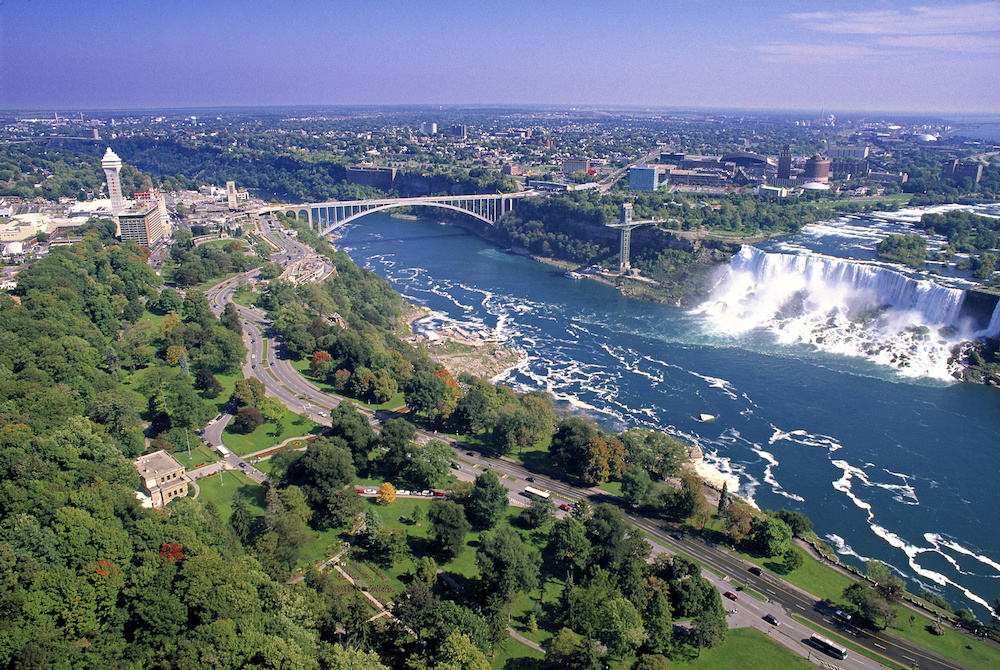 overview of niagara with green trees, waterfalls, bridge and city
