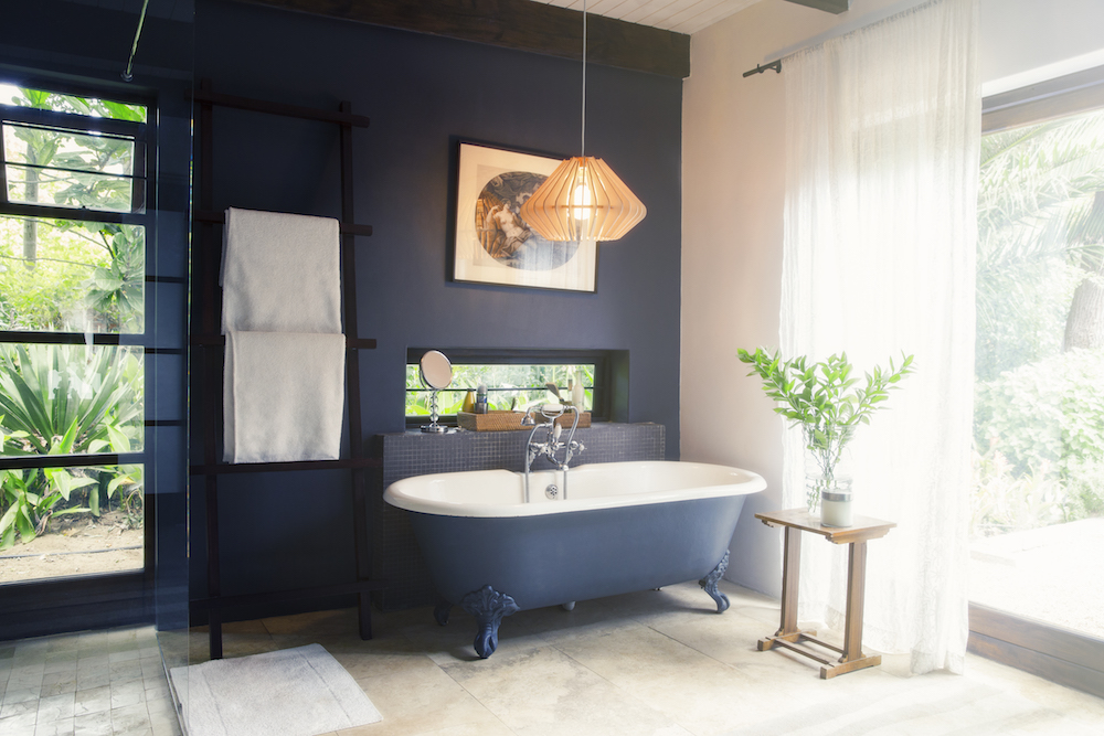 navy blue bathroom with freestanding bathtub and windows with green plants outside
