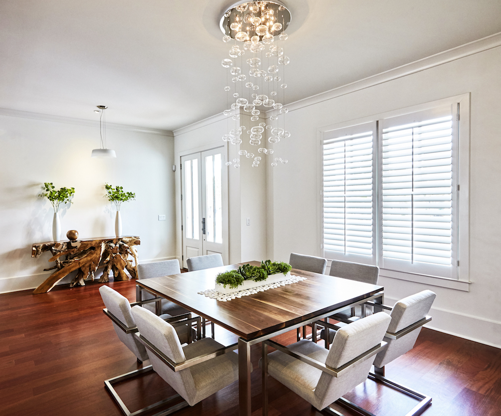 delicate glass light fixture hanging over wooden dining table in white room