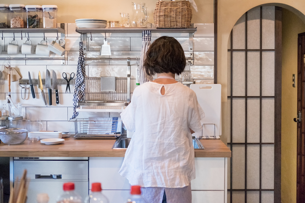 woman in white kitchen with silver utensil racks on while-tile wall