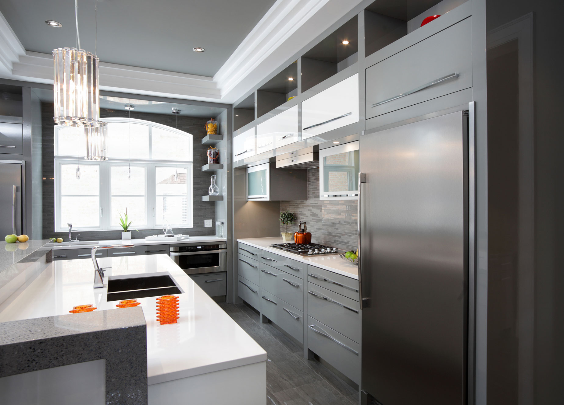 A brightly lit grey kitchen with steel fridge and while marble countertops