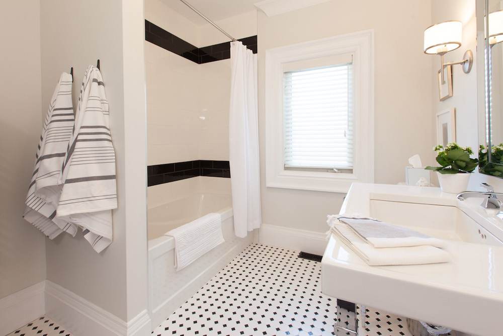 white bathroom with black tile accents and striped towels hanging from towel hooks