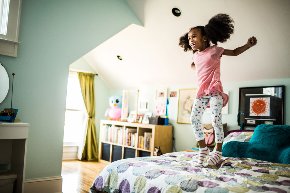 girl jumping on bed in pastel-coloured room