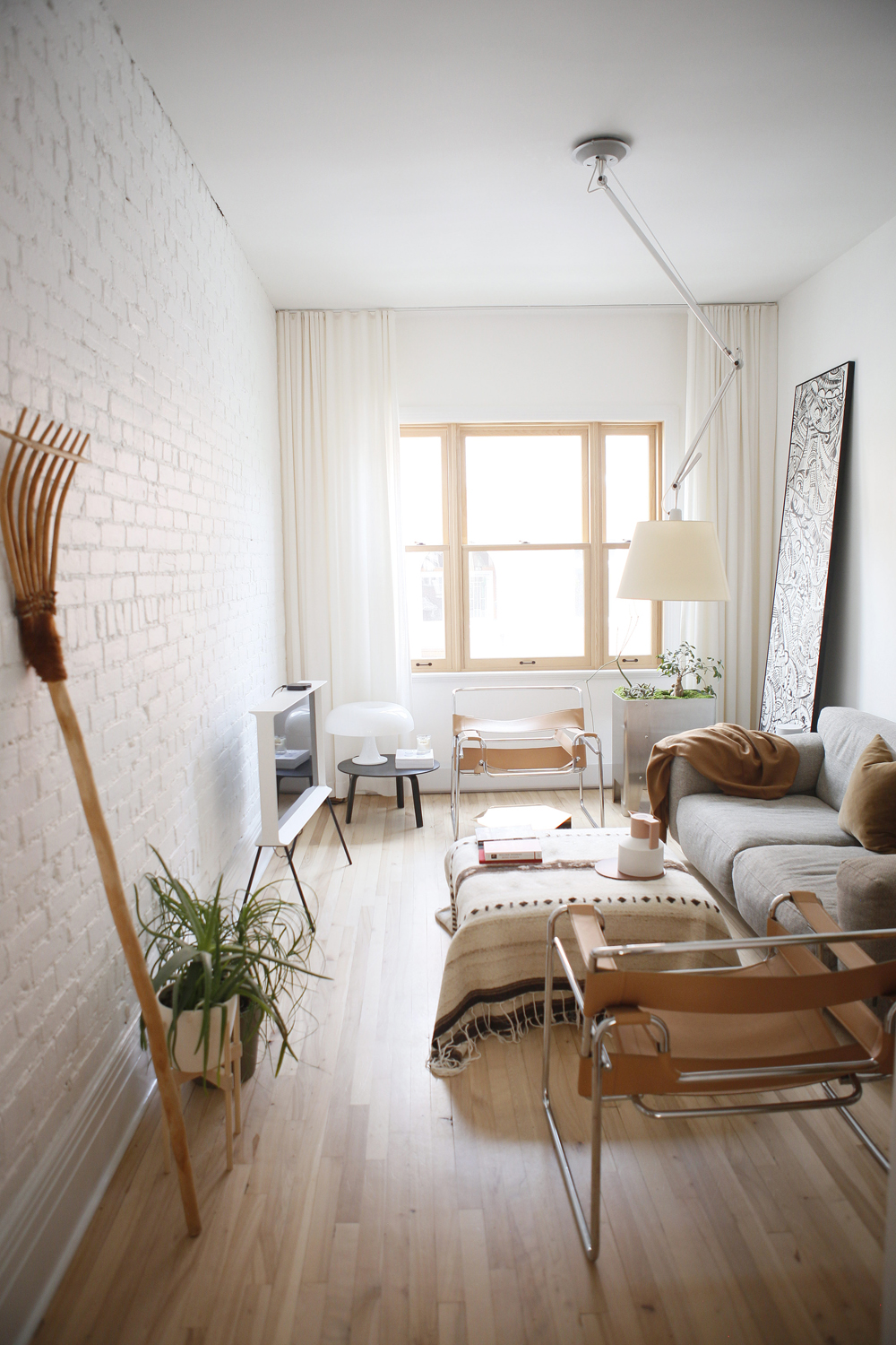 Narrow white living room with white brick wall and rake on left