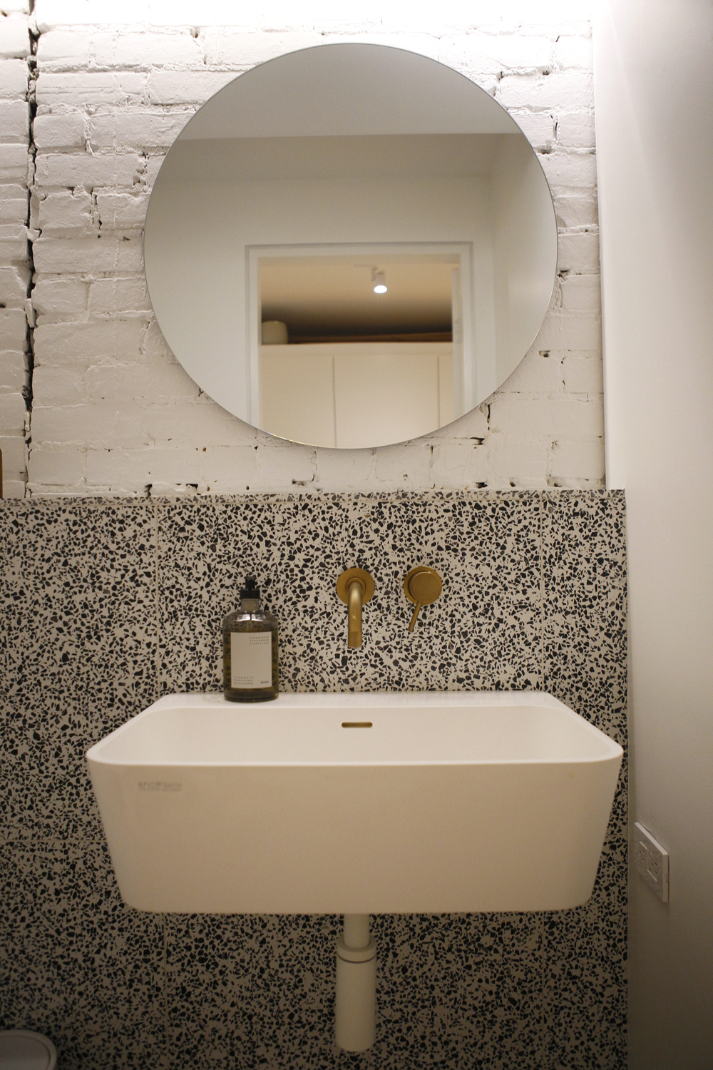 bathroom sink, round mirror, black and white terrazzo, white bricks
