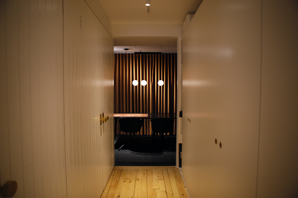 white hallway wood floors leading to dark space with three bulb chandelier