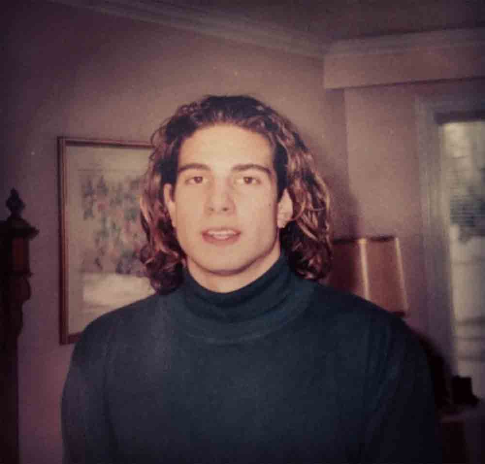 A young Scott McGillivray with long wavy hair and a turtleneck.