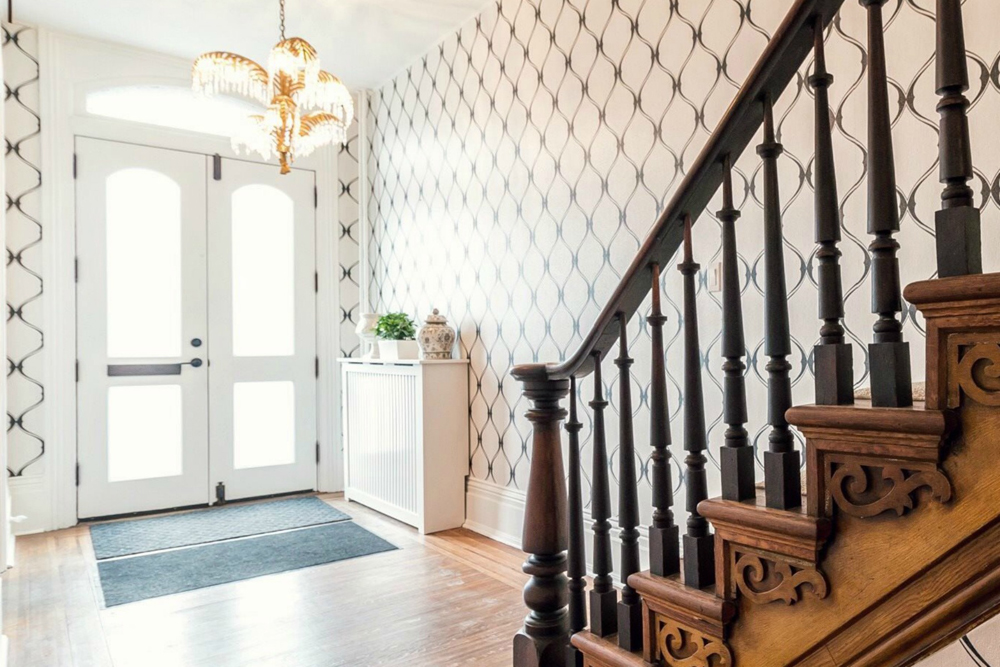 Beautifully styled residential home entrance way with wood staircase and contemporary painted design on feature wall.