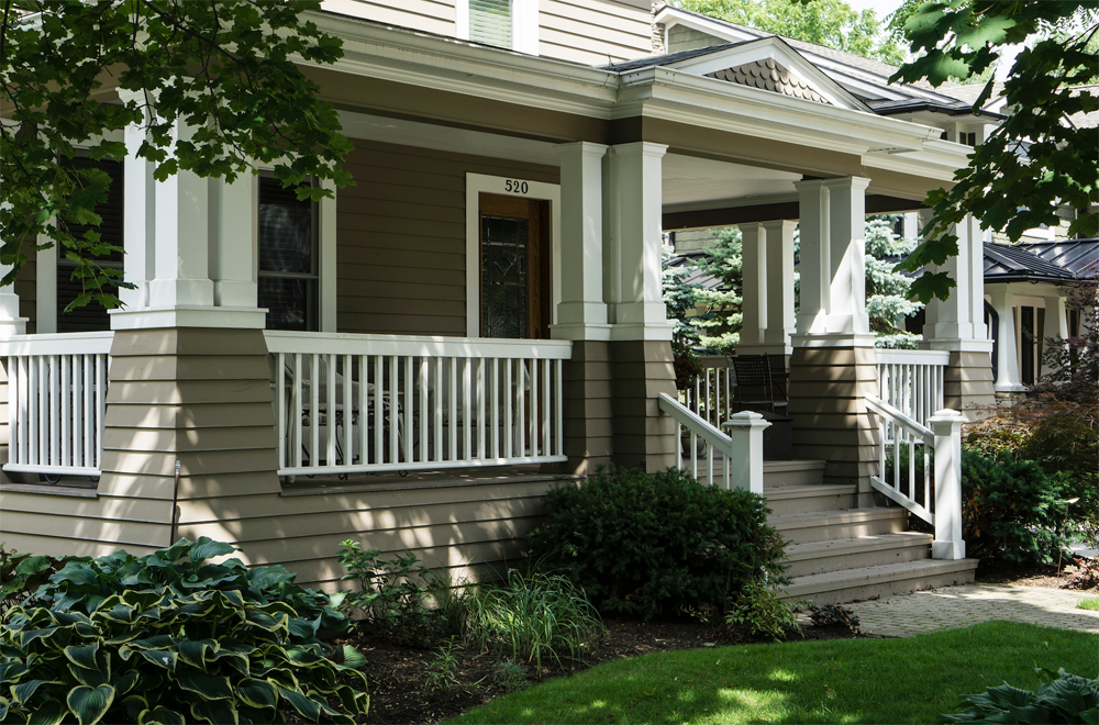 Beautiful residential home with a large porch and white railing, with taupe-coloured siding.
