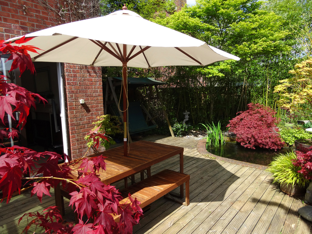 Image of garden decking with table and benches, cream-parasol, red-maples.
