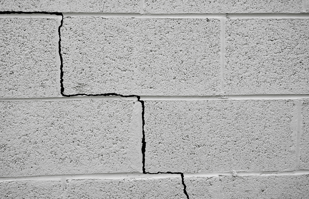 A close-up of a grey cement wall with a very large crack going through the centre.