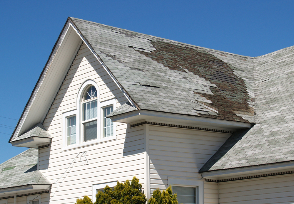 A roof shown with discoloured and falling off roof shingles.
