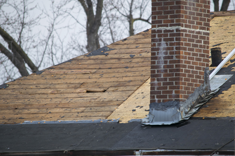 Damaged and old roofing shingles around an old brick chimney that is duck-taped to the roof.