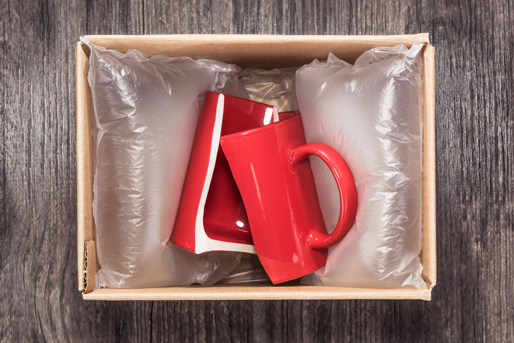 A small cardboard box with a red ceramic mug in it, which is broken in two.