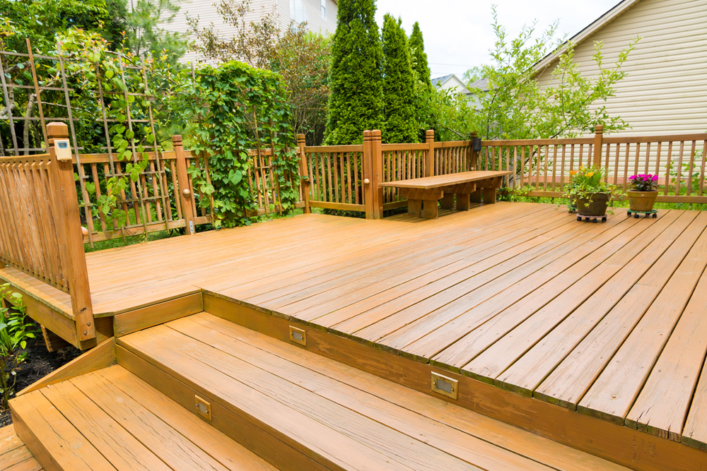 Gorgeous wood-stained backyard deck with stairs, and lots of greenery and potted plants featured in the background.