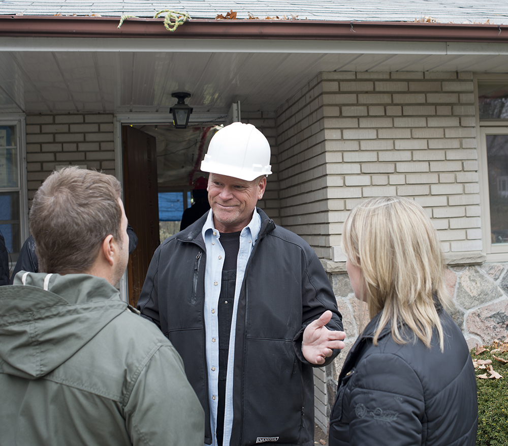 Mike Holmes standing in front of a house talking to two people