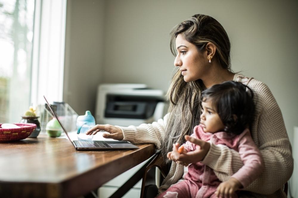 A woman researching general contractors on her laptop, holding her baby girl