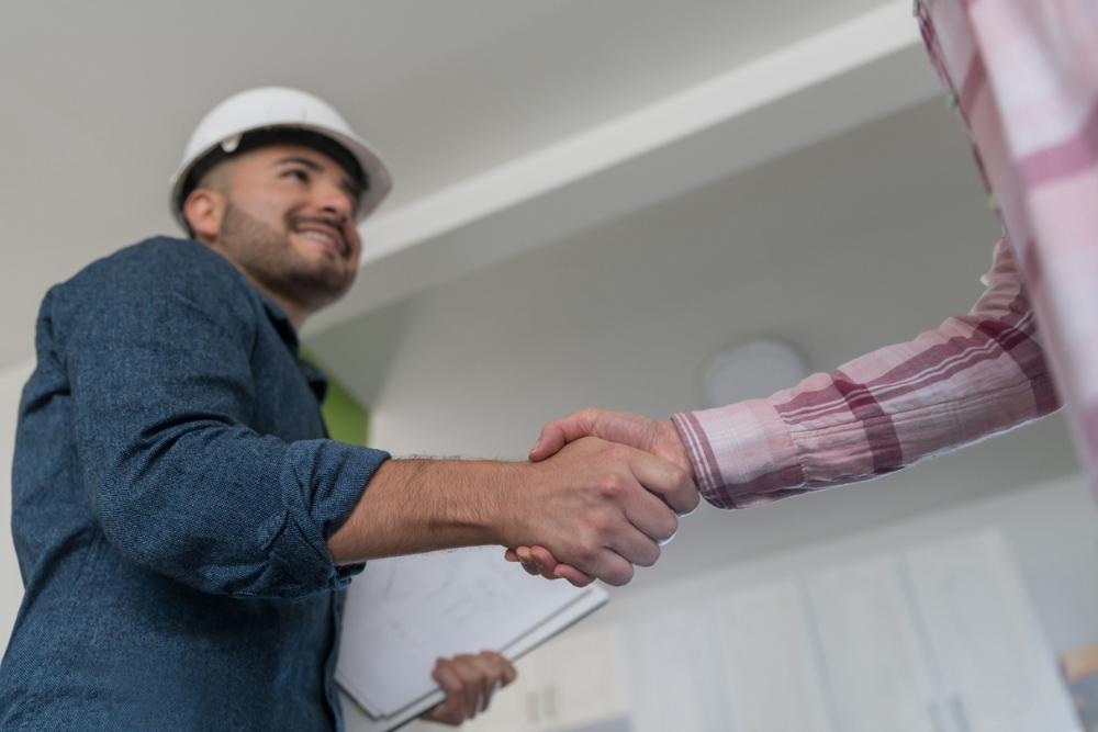 A man shaking hands with a general contractor in a hard hat holding a clipboard