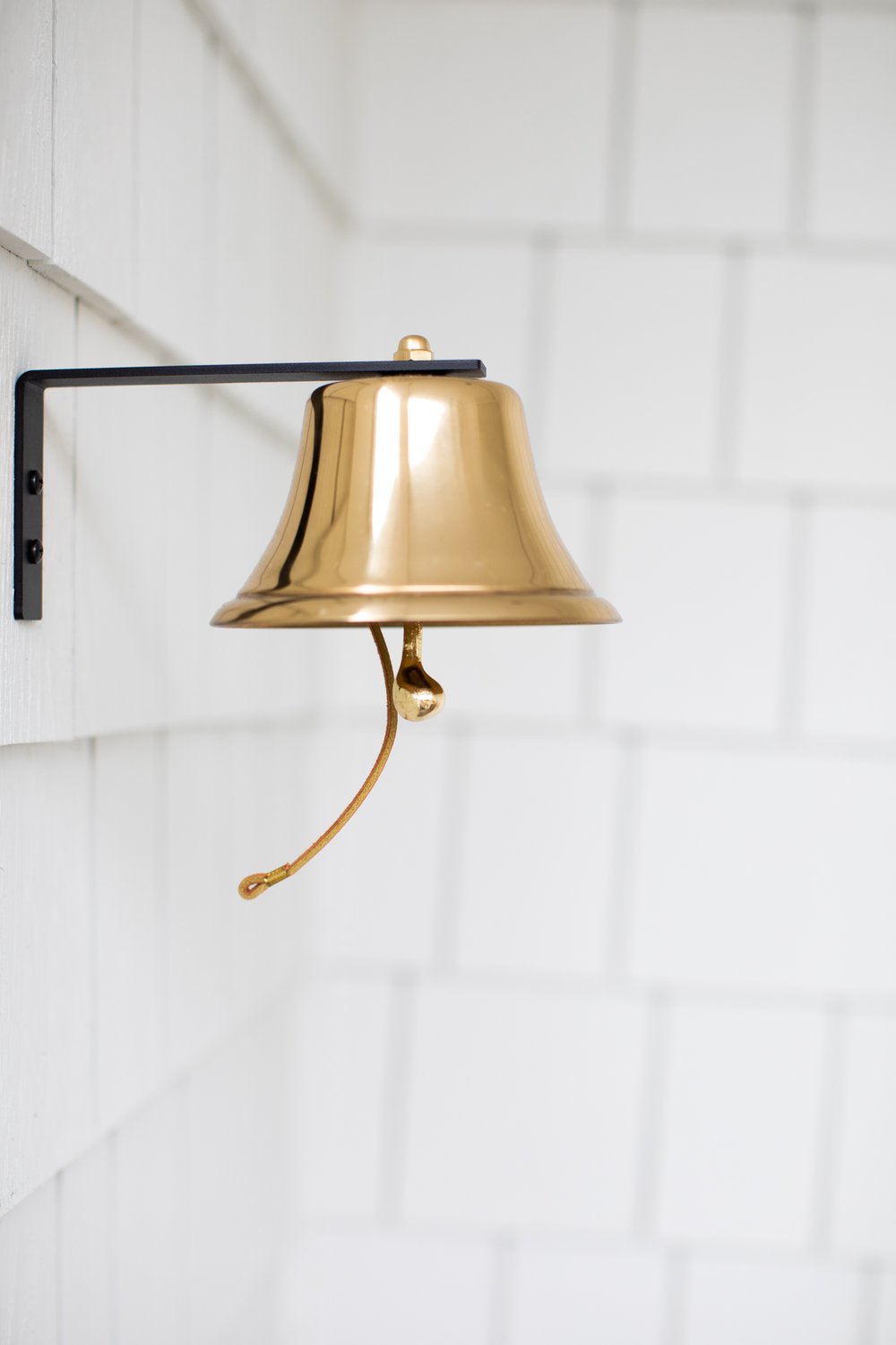 Brass bell hanging outside white shingled home