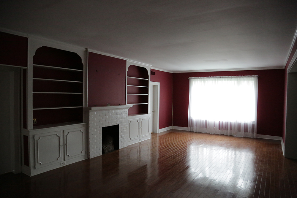 Bare formal living room with red walls and a white brick fireplace