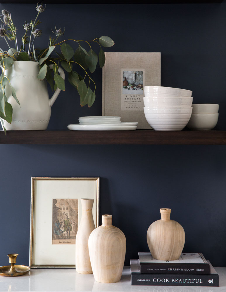 Rustic open wood shelves in kitchen with navy blue accent wall and vintage accessories.