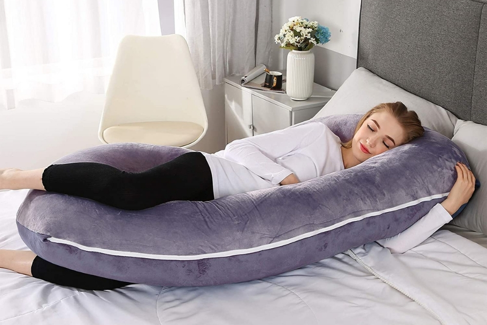 A woman smiling in her sleep using a purple pregnancy pillow.