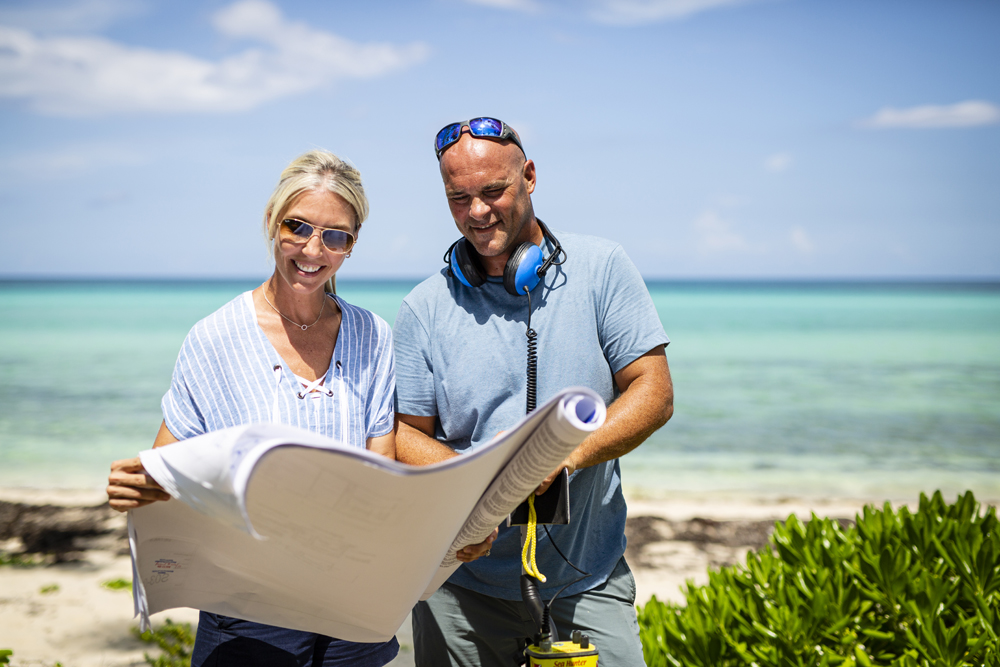 Sarah and Bryan Baeumler holding a map near their renovation project in the Bahamas