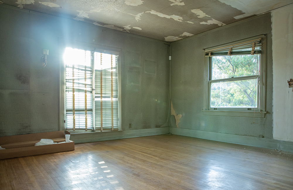 A run-down bedroom with broken window shades and faded teal walls