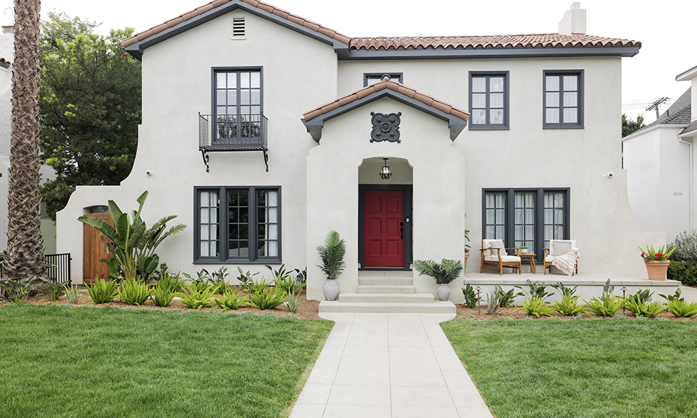 A newly renovated front of a home with new stucco, trim and red door.