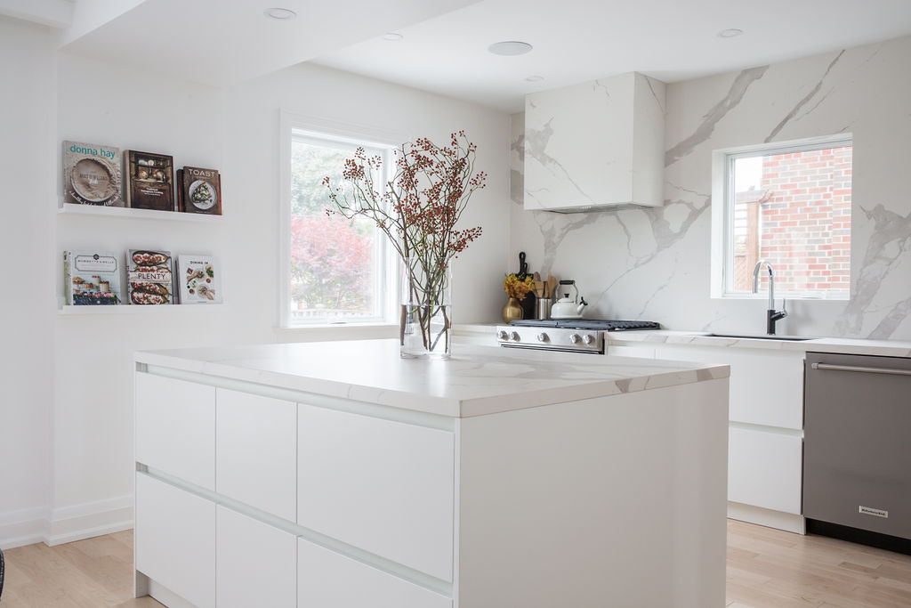 Clean, white kitchen with white marble countertops and island with substantial cabinetry