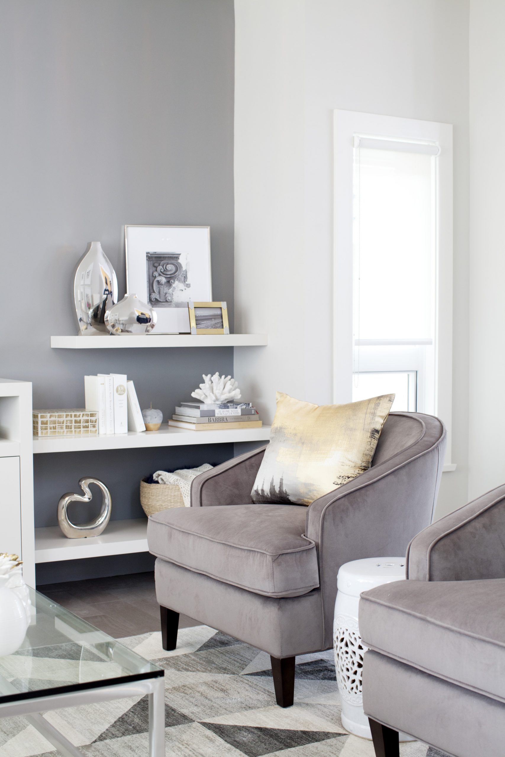 one grey wall with white shelves and two grey velvet armchairs