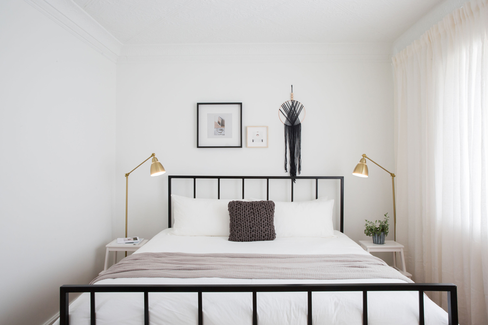 black bed frame in white room with brass floor lamps