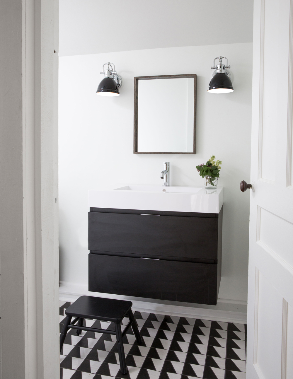black and white bathroom with two black drawer floating vanity, white sink, black stool, black and white floor