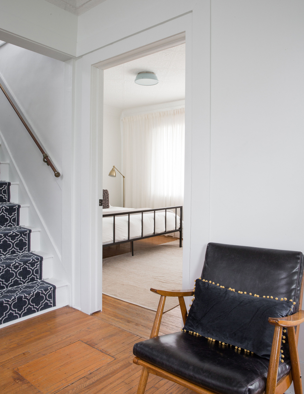 landing with black leather chair, black and white stair runner, looking into bedroom