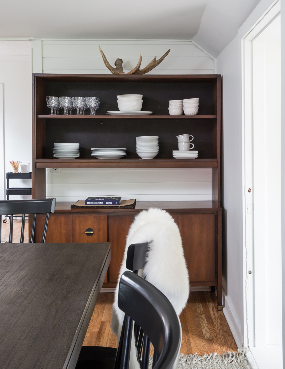 wooden shelving unit in dining room with white dishes and antlers on top
