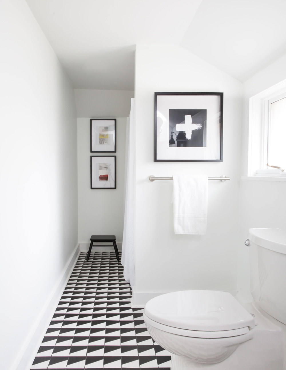 white bathroom with black and white floor, three black framed artwork