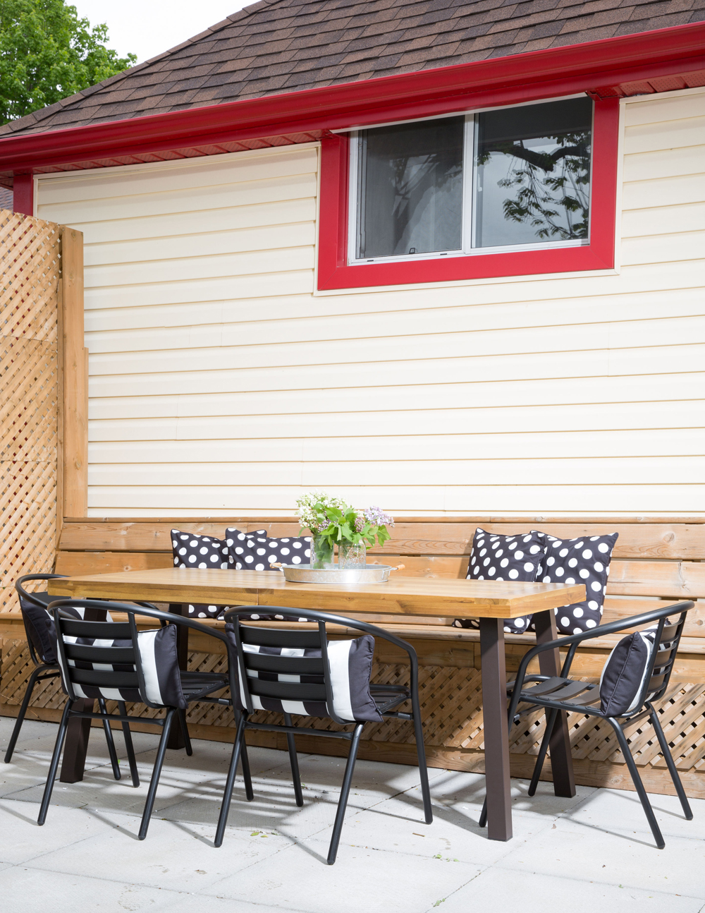 outdoor table, wooden bench, black chairs, black and white dot cushions, red trim on house exterior