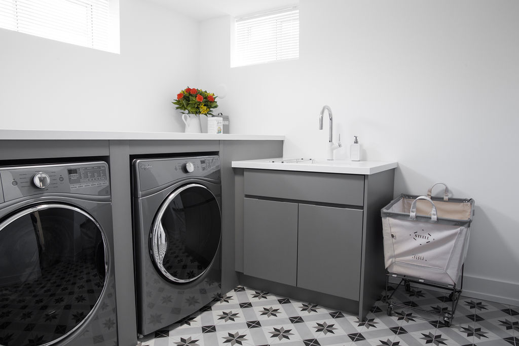 Dual washer dryer surrounded by tile and grey cabinets